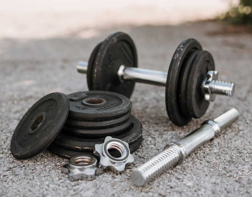 Heavy adjustable dumbbell near cast iron plates and hexagonal collars with stainless steel bar on pavement