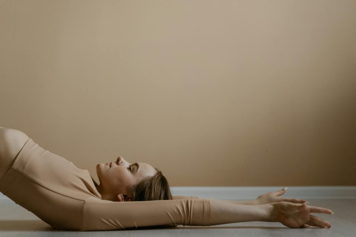 Woman in calm yoga pose, arms extended, in neutral setting.
