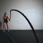 A focused woman performs a dynamic battle rope exercise in a gym setting, demonstrating strength and fitness.