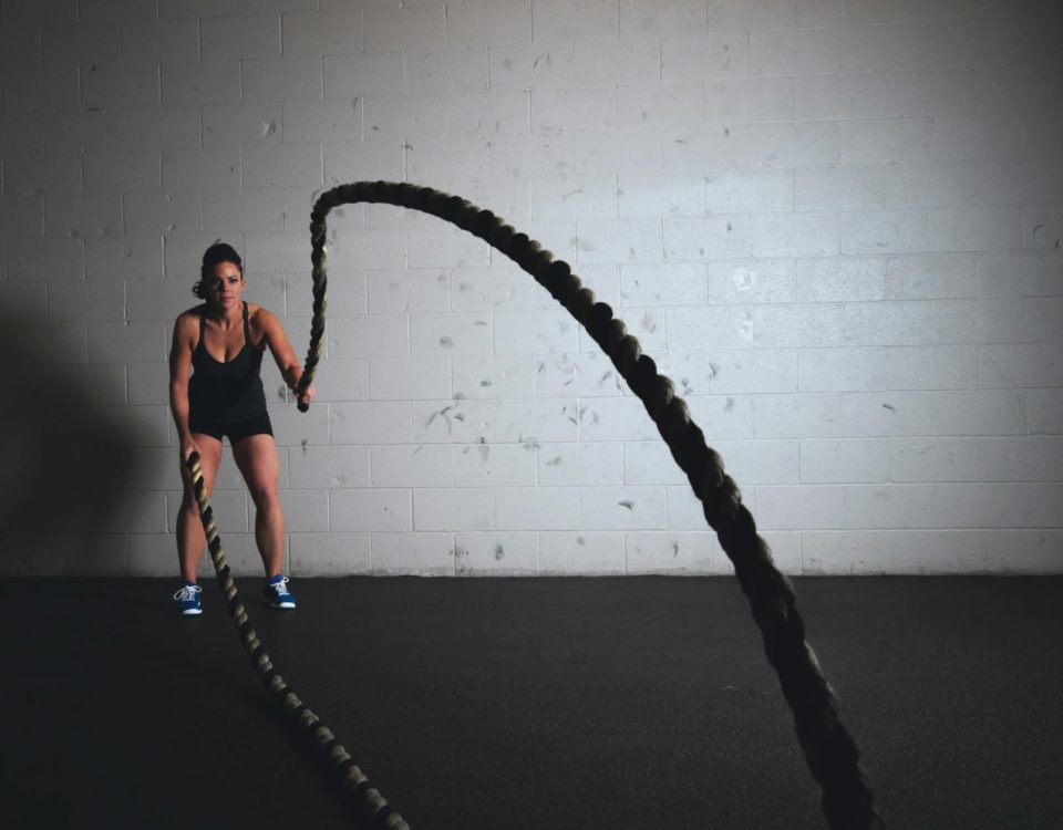 A focused woman performs a dynamic battle rope exercise in a gym setting, demonstrating strength and fitness.
