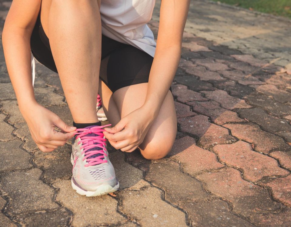 Adult woman tying pink laces on running shoes outdoors. Focuses on fitness and lifestyle.