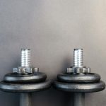 Close-up of two iron dumbbells on a gray background, perfect for strength training images.