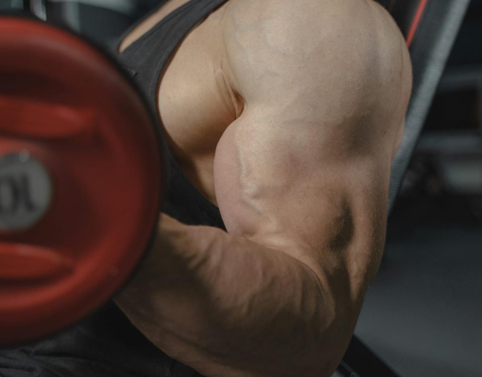 A focused view of a bodybuilder's arm muscles lifting a dumbbell in a gym setting.