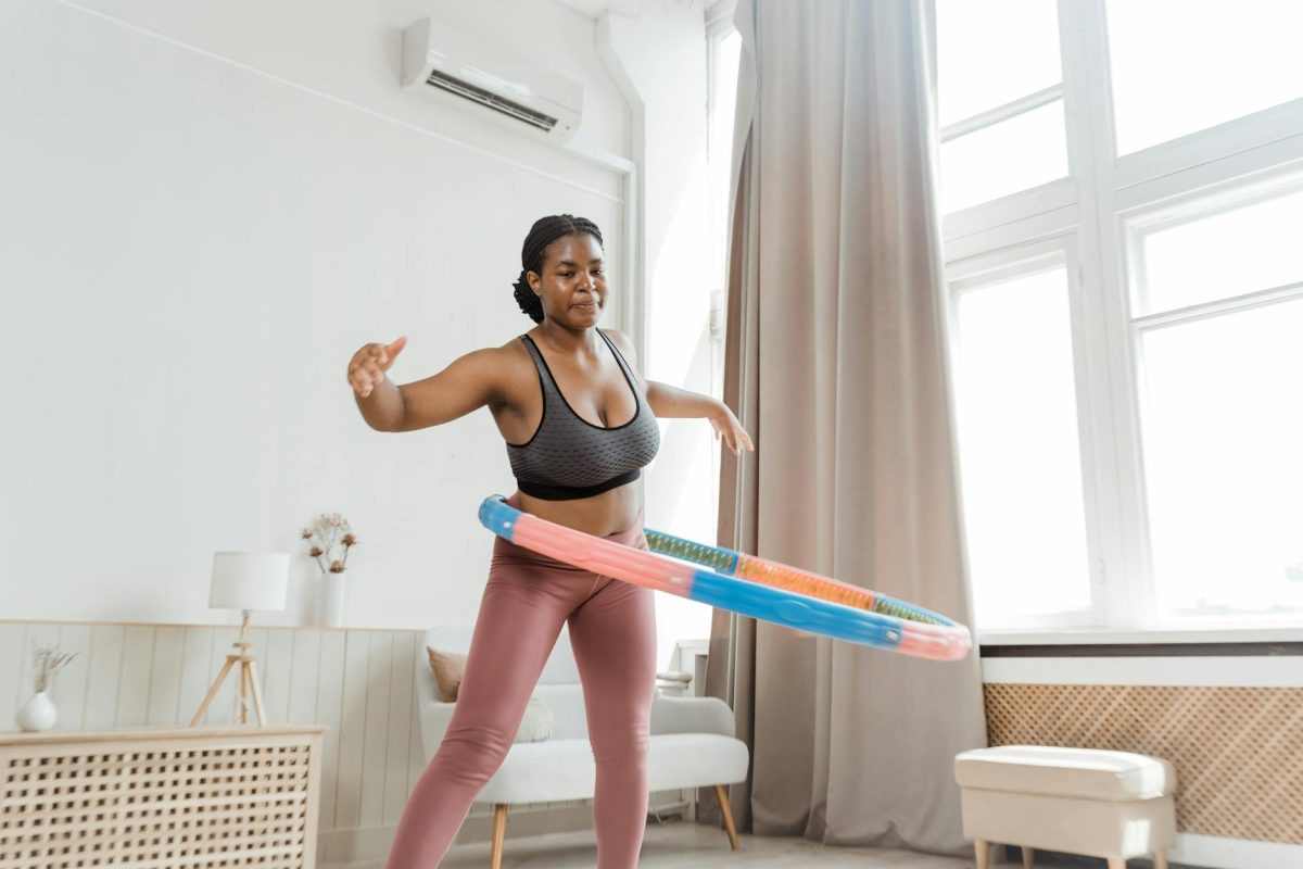 Black woman hula hooping at home, showcasing indoor fitness and health.