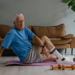 Elderly man enjoys a healthy lifestyle by exercising indoors on a yoga mat with weights.