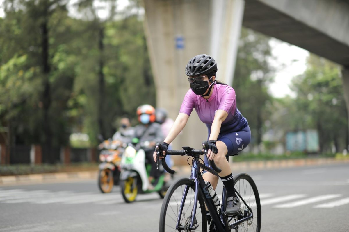 Woman wearing a mask and helmet cycling in Jakarta amidst pandemic.