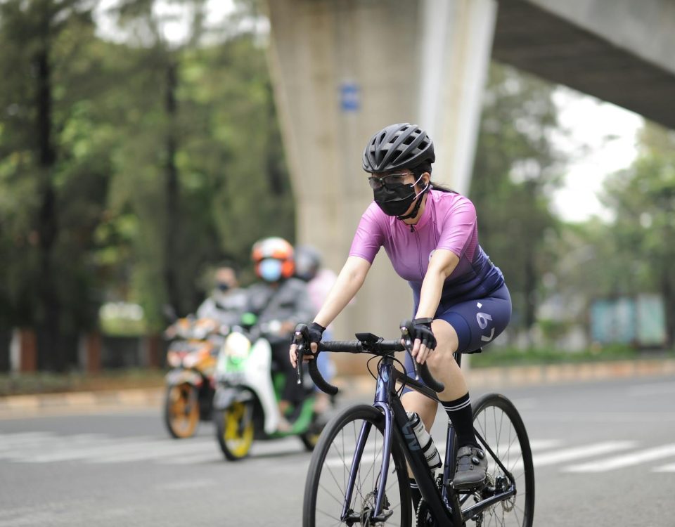 Woman wearing a mask and helmet cycling in Jakarta amidst pandemic.