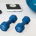 Blue dumbbells placed on a white surface with fitness equipment in the background.