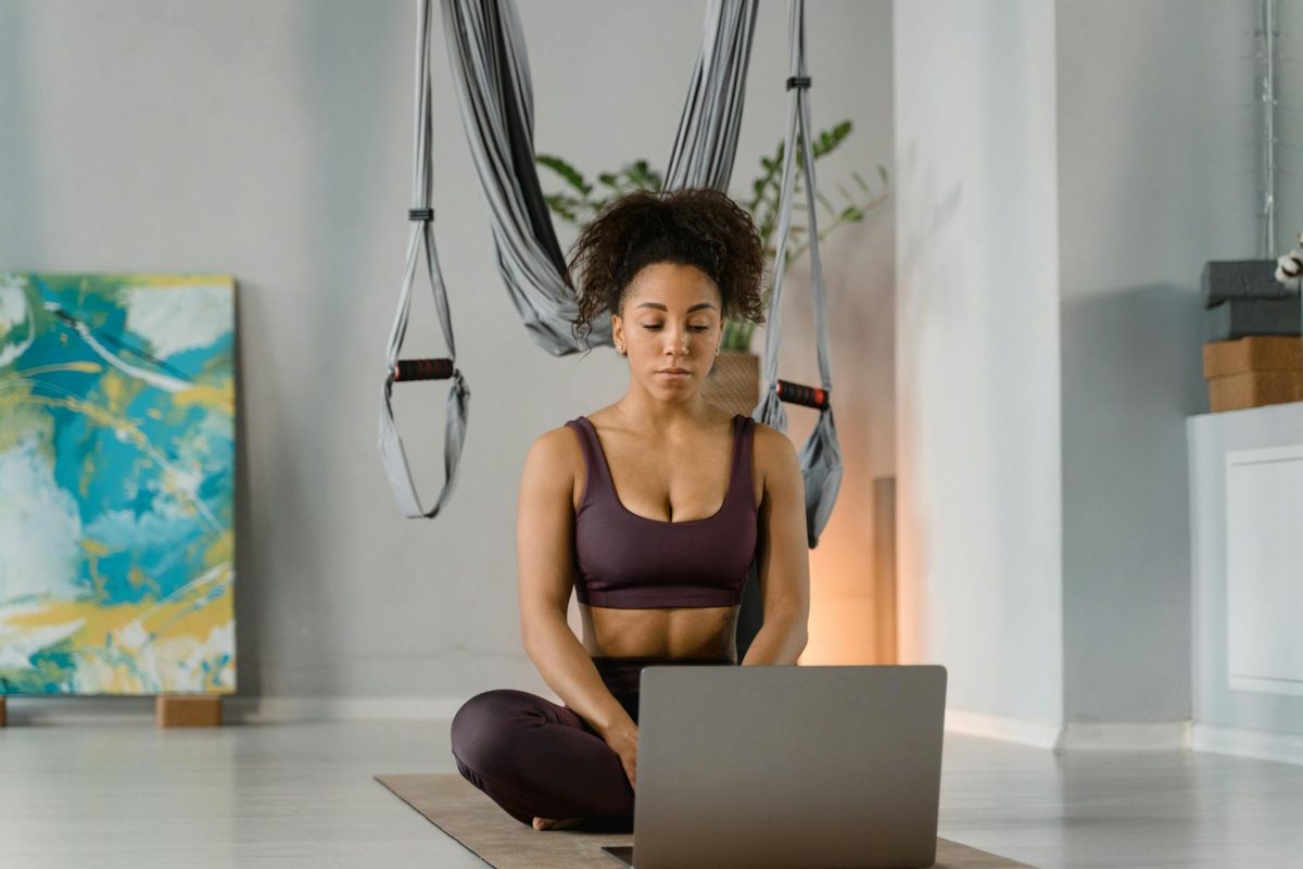 A woman practicing yoga at home with a laptop, focusing on fitness and mindfulness.