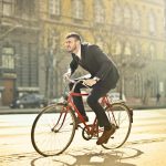 Businessman in suit riding a red bicycle on a bright city street, embodying urban commute.