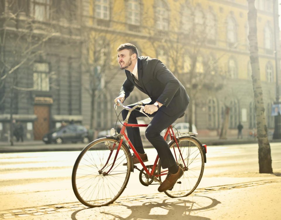 Businessman in suit riding a red bicycle on a bright city street, embodying urban commute.