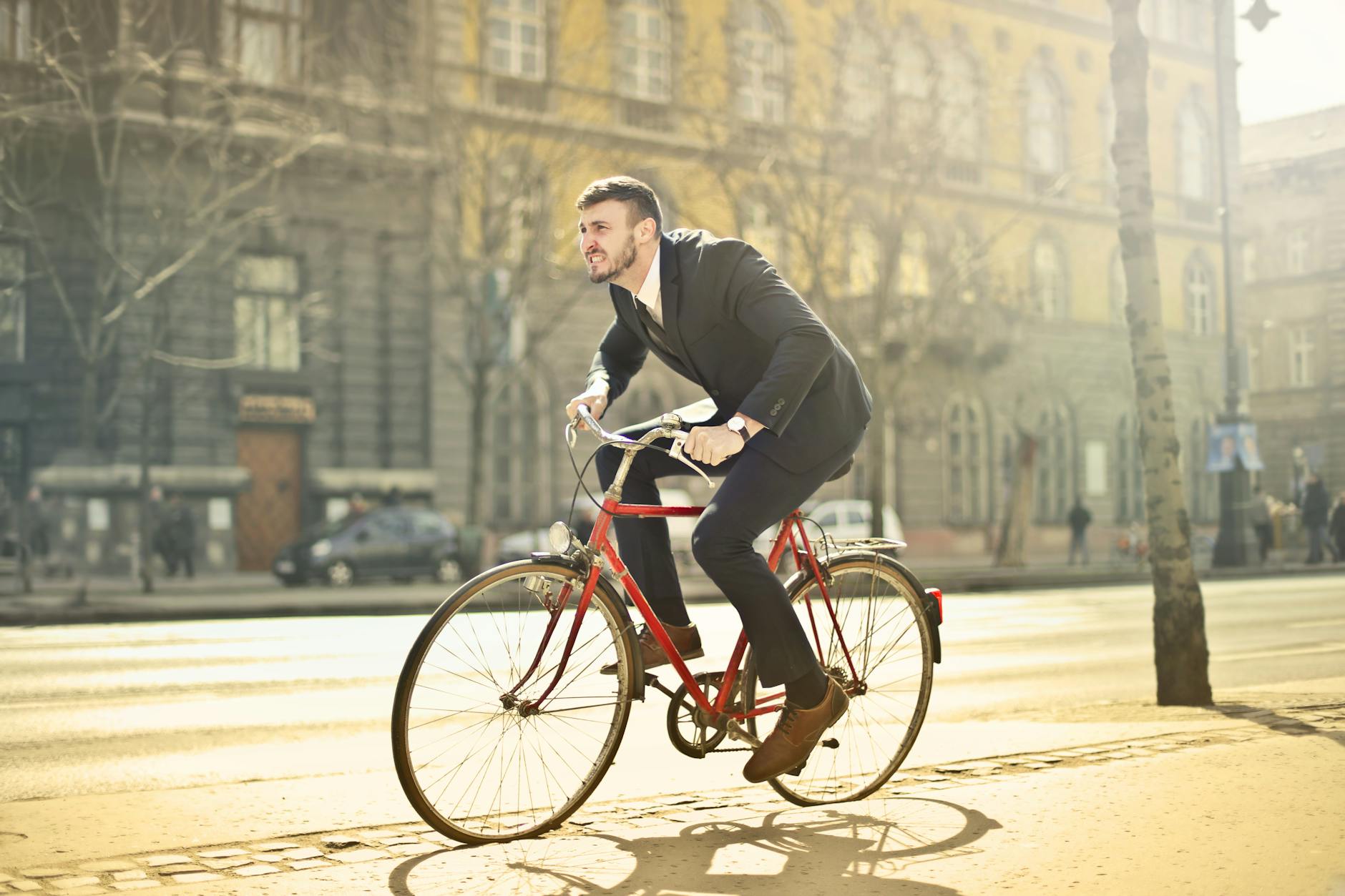 Businessman in suit riding a red bicycle on a bright city street, embodying urban commute.