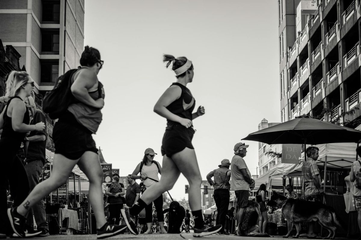 Black and white photo of people jogging and walking in a lively city street.
