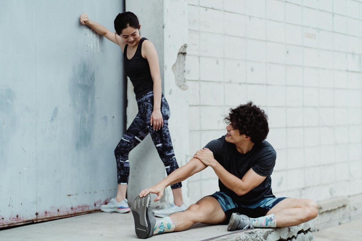 Two adults in sportswear stretching against a wall outdoors, embracing fitness and a healthy lifestyle.