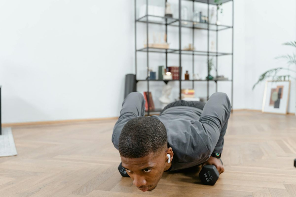 African American man performing push-ups using dumbbells indoors, emphasizing fitness and a healthy lifestyle.
