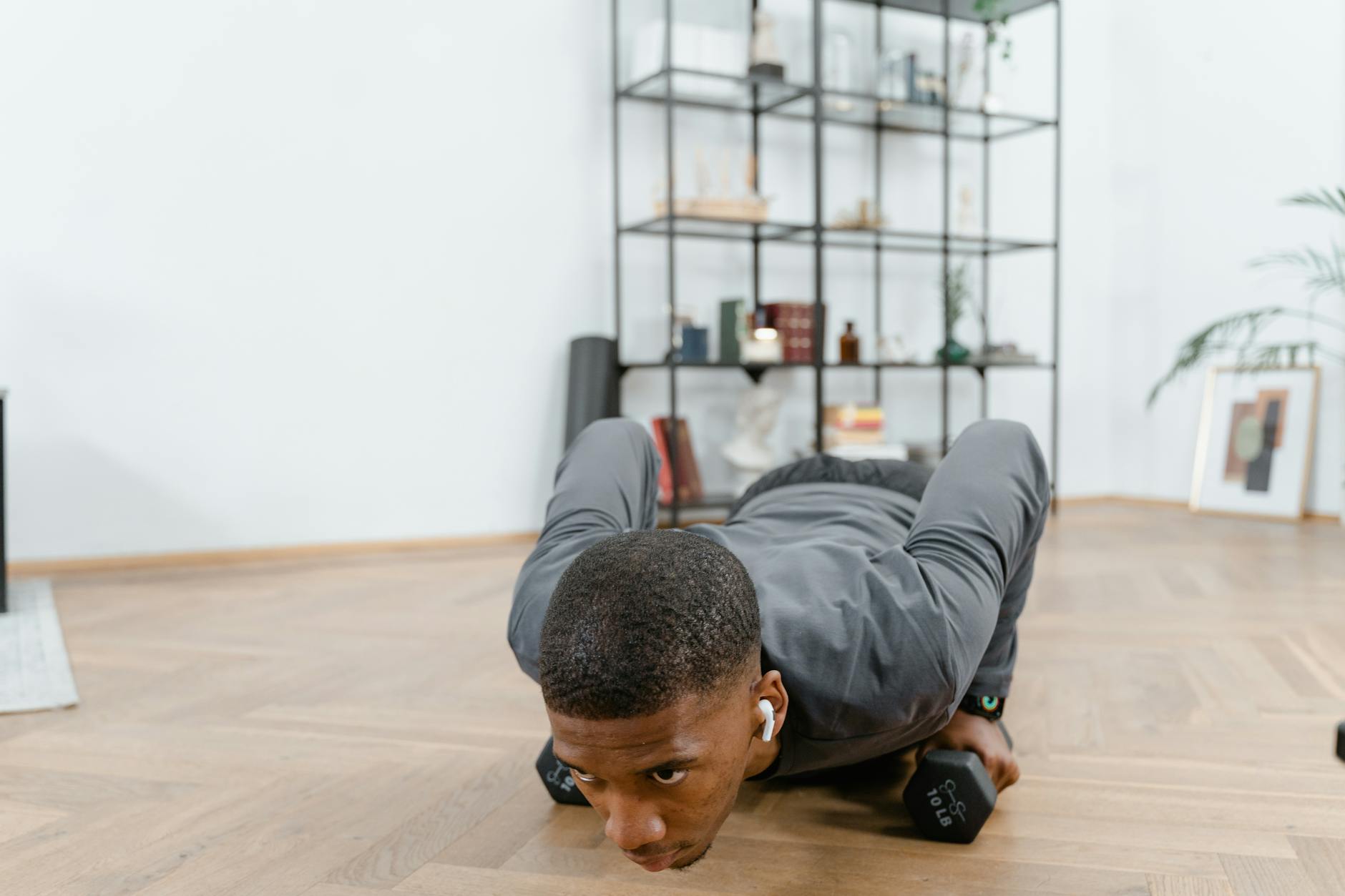 African American man performing push-ups using dumbbells indoors, emphasizing fitness and a healthy lifestyle.