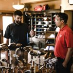 Two men browsing golf clubs in a sports equipment store, discussing options.