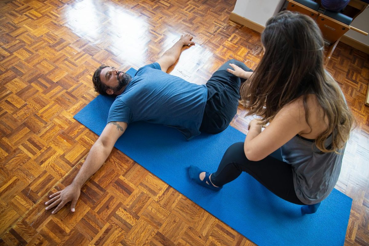 A man and woman engaged in a rehabilitation exercise on a yoga mat indoors.