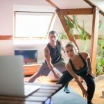 A man and woman working out at home using a laptop for guided exercises. Indoor active lifestyle.
