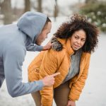 Black personal trainer pointing away and touching shoulder of plump African American female during training in snowy park on blurred background