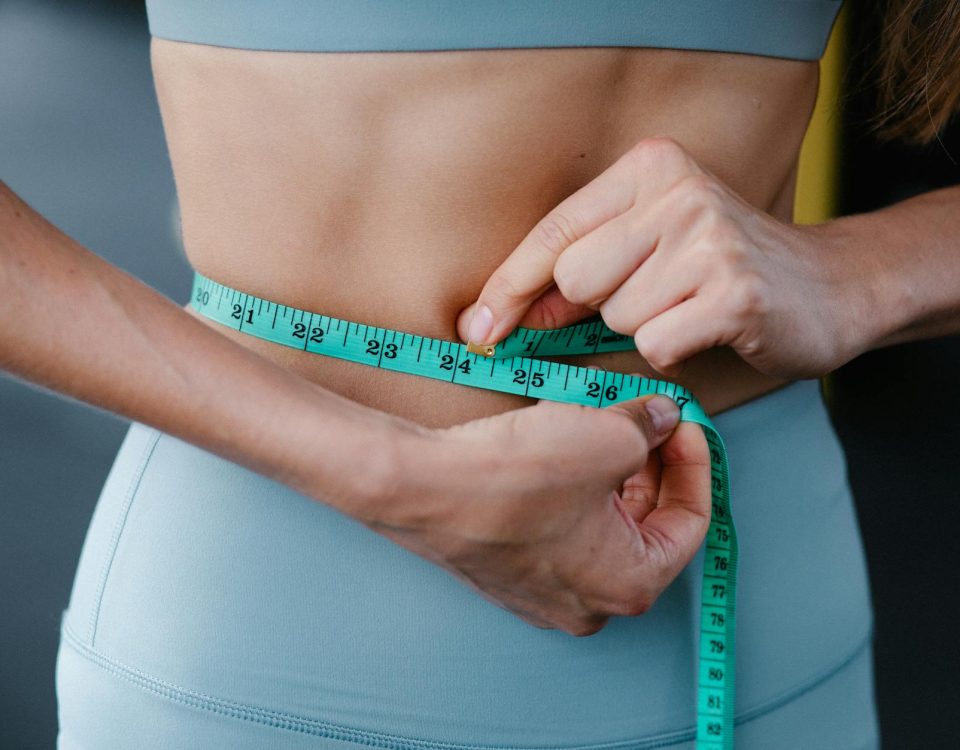 Close-up of a woman measuring her waist with a tape, representing fitness, health, and weight loss.