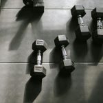 Hexagonal dumbbells on a gym floor bathed in natural sunlight, creating dynamic shadows.