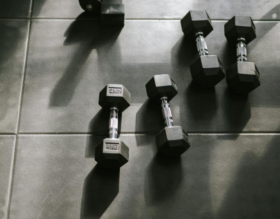 Hexagonal dumbbells on a gym floor bathed in natural sunlight, creating dynamic shadows.