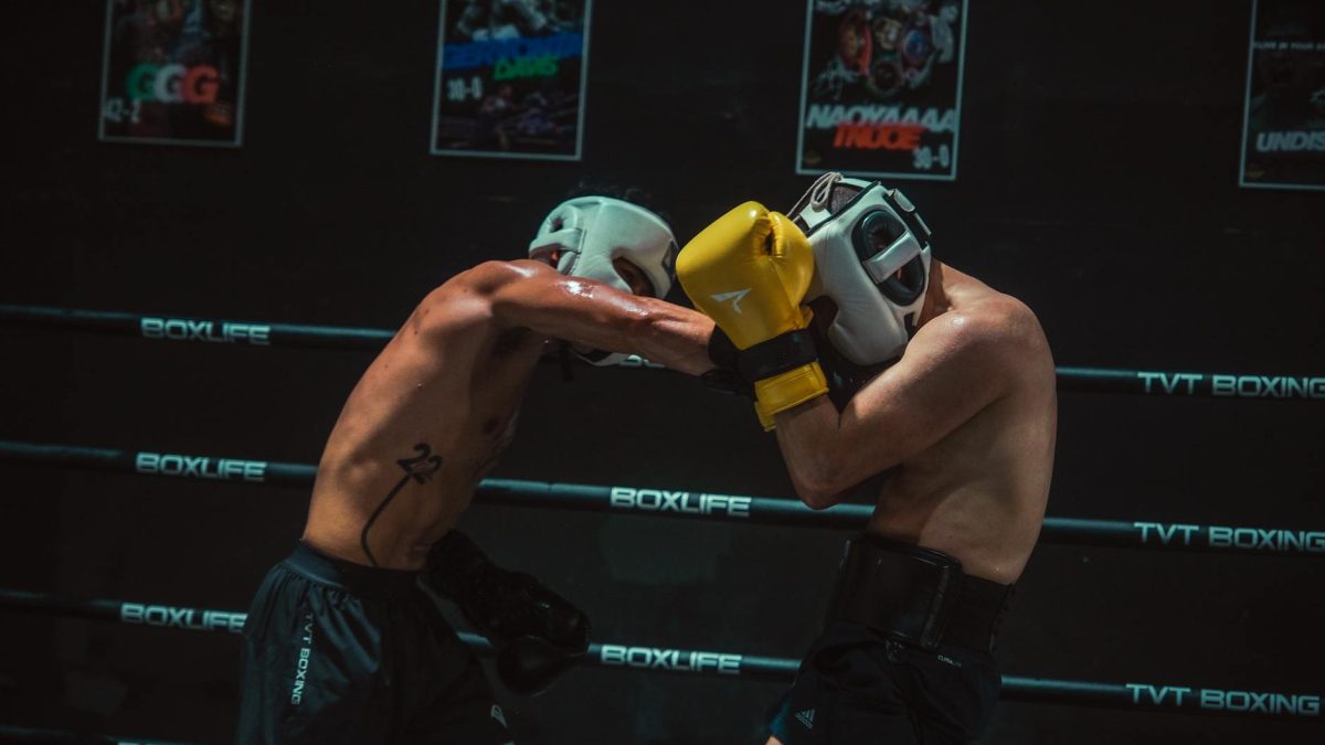 Two boxers sparring intensely in a dimly lit boxing gym with protective gear.