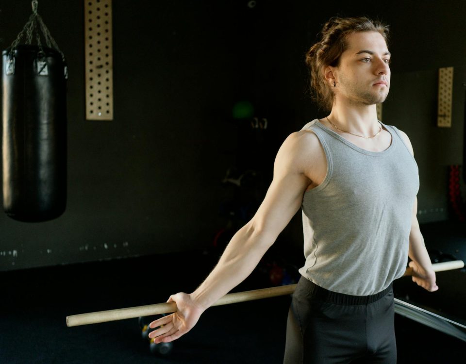 A man in a gym stretching with a rod next to a punching bag, emphasizing fitness and concentration.