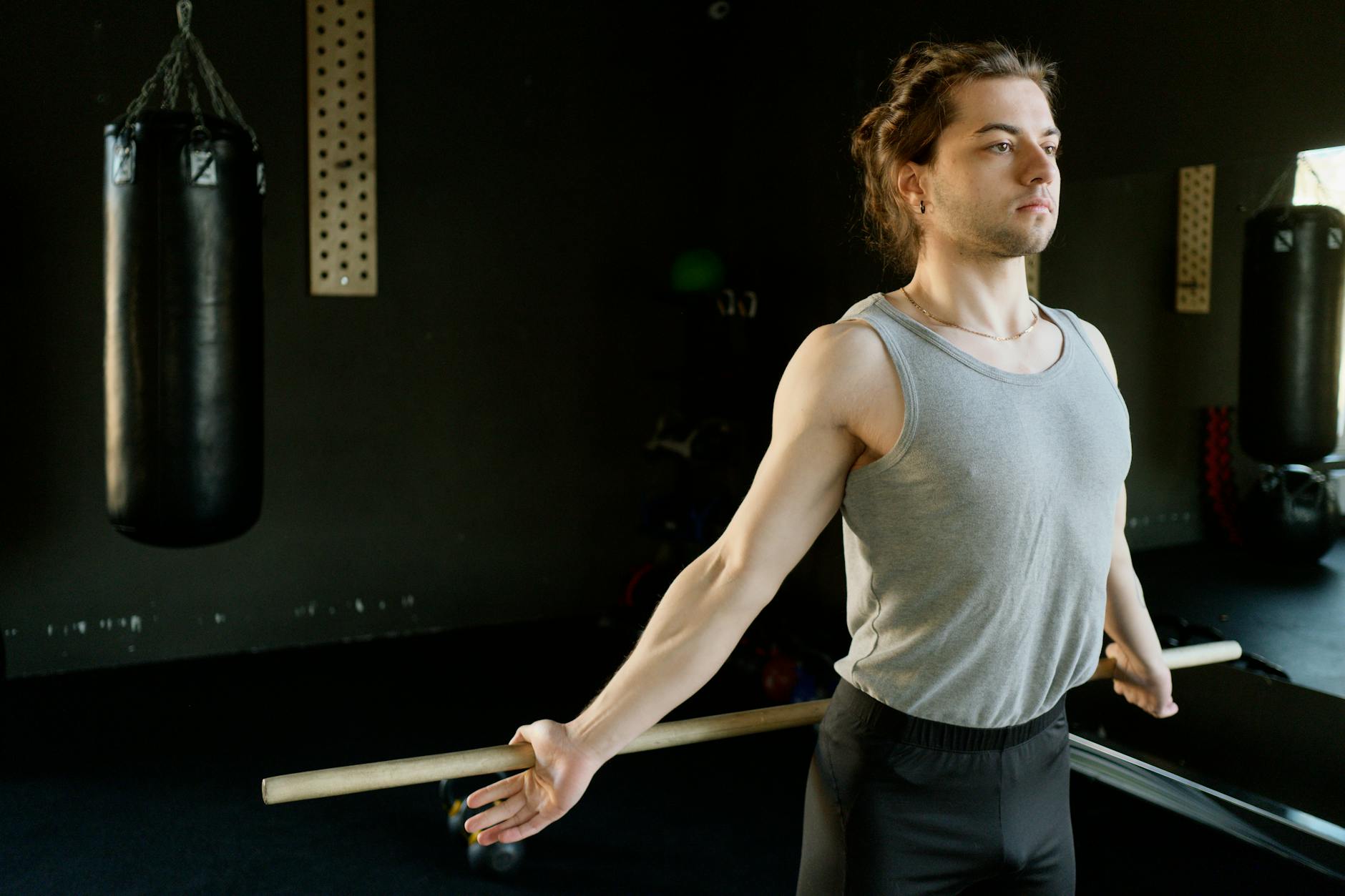 A man in a gym stretching with a rod next to a punching bag, emphasizing fitness and concentration.