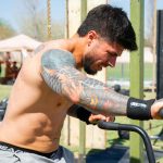 Focused male athlete with tattoos working out on an assault bike outdoors.