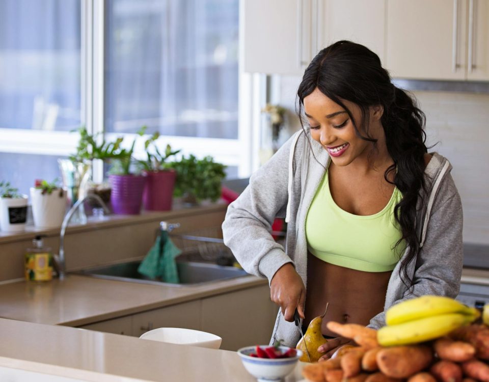 Smiling woman preparing fresh fruit in a sunlit kitchen, embodying a healthy lifestyle.