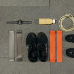 Flat lay of workout essentials including sneakers, bands, watch, rope, and healthy drink.