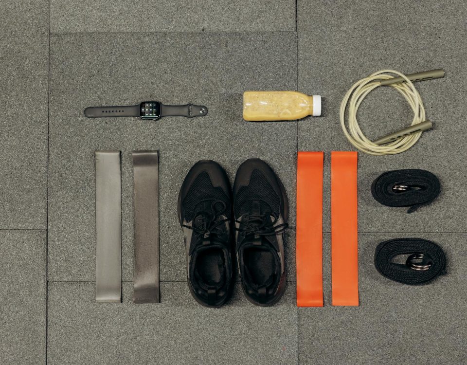 Flat lay of workout essentials including sneakers, bands, watch, rope, and healthy drink.