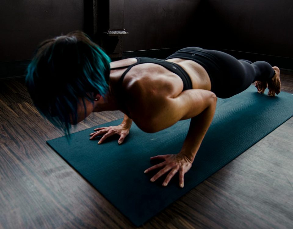 A fit woman with blue hair performs a push-up on a yoga mat indoors, showcasing strength and focus.