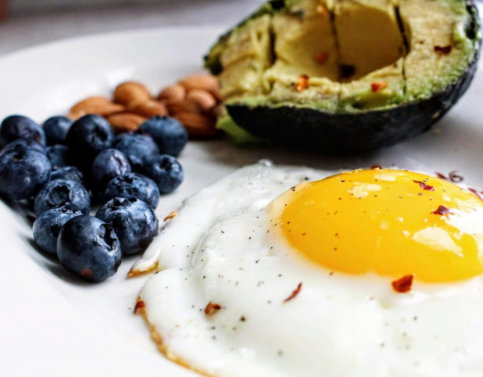 A nutritious breakfast featuring a fried egg, avocado, blueberries, and almonds.
