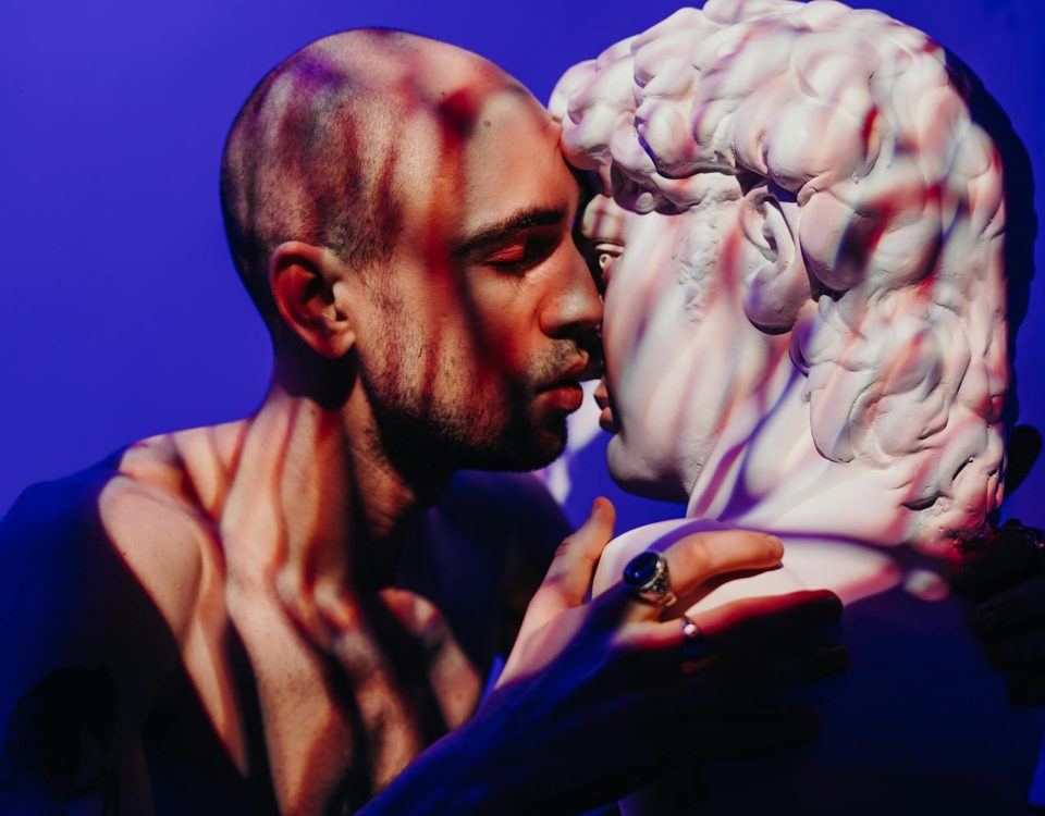 A man intimately engages with a sculpture, exploring themes of self-love and connection.