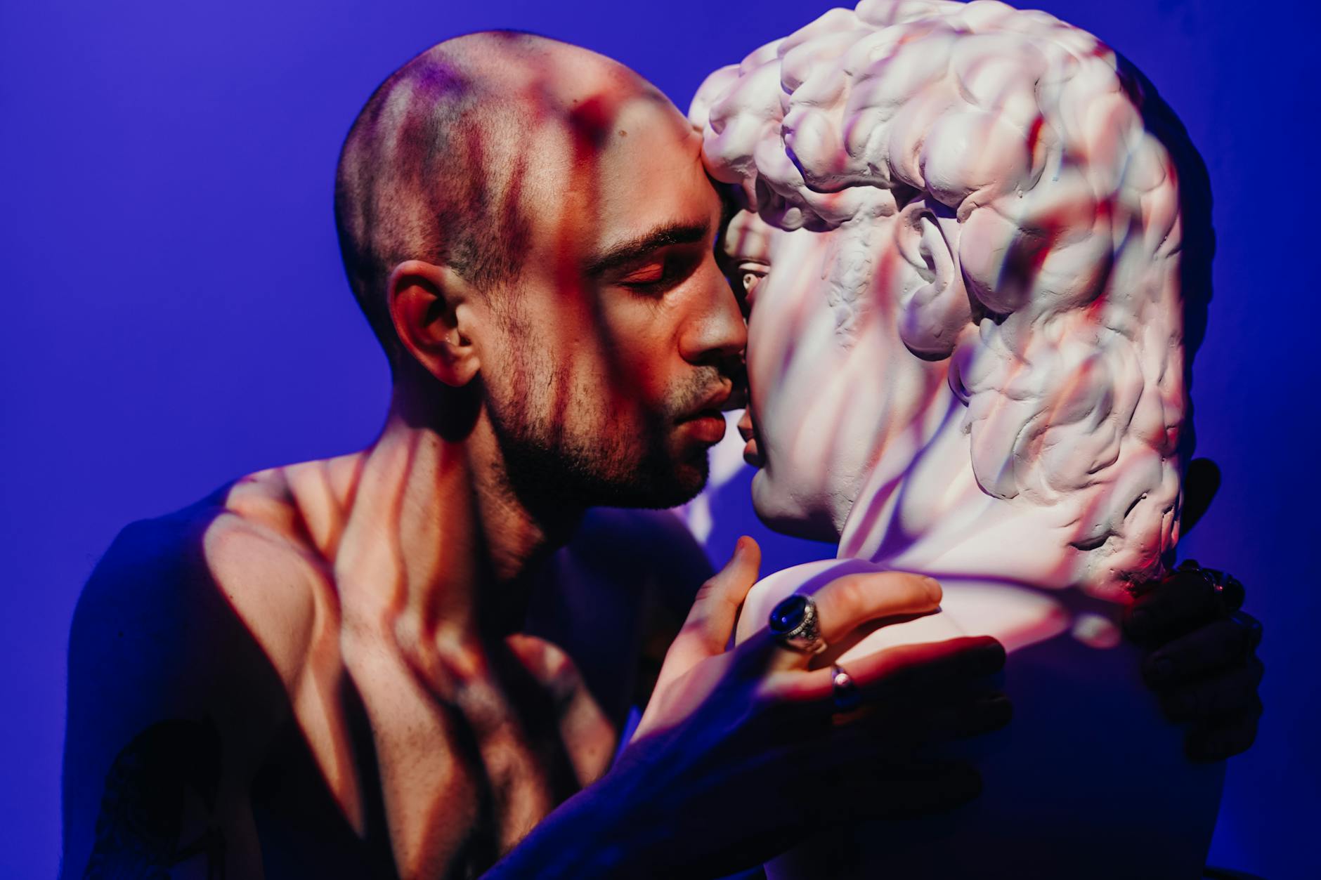 A man intimately engages with a sculpture, exploring themes of self-love and connection.