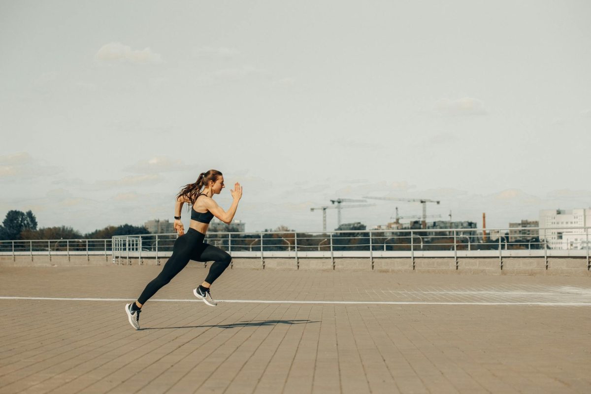 Woman sprinting on a rooftop in athletic wear during the day.