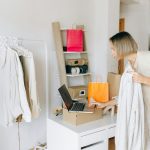 A woman in casual attire unpacking a delivery box with clothing at home, engaging in online shopping.