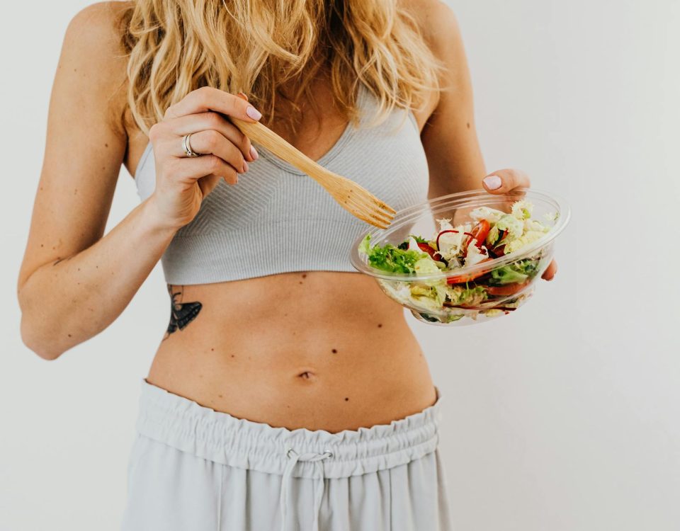 Young woman in sports attire holding a fresh salad bowl, promoting a healthy lifestyle.