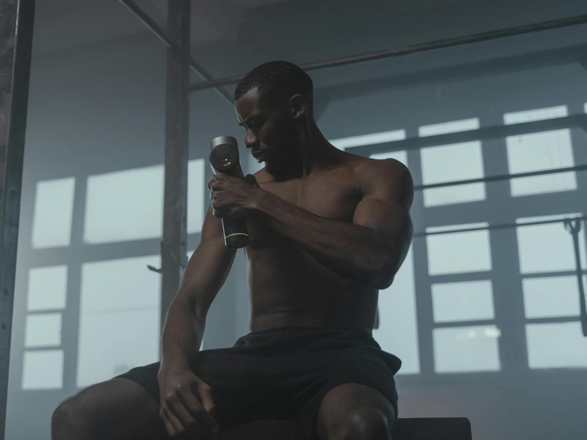 A dedicated athlete uses a massage gun to relax his muscles post-workout in the gym.