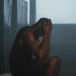 Sweaty man resting on bench in dimly lit locker room, showing exhaustion and recovery.