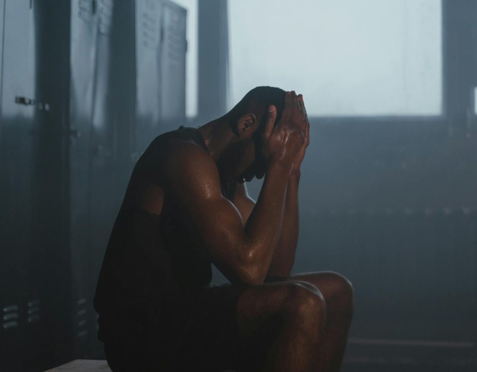 Sweaty man resting on bench in dimly lit locker room, showing exhaustion and recovery.
