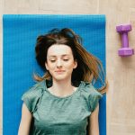 A young woman peacefully resting on a yoga mat with dumbbells beside her indoors.