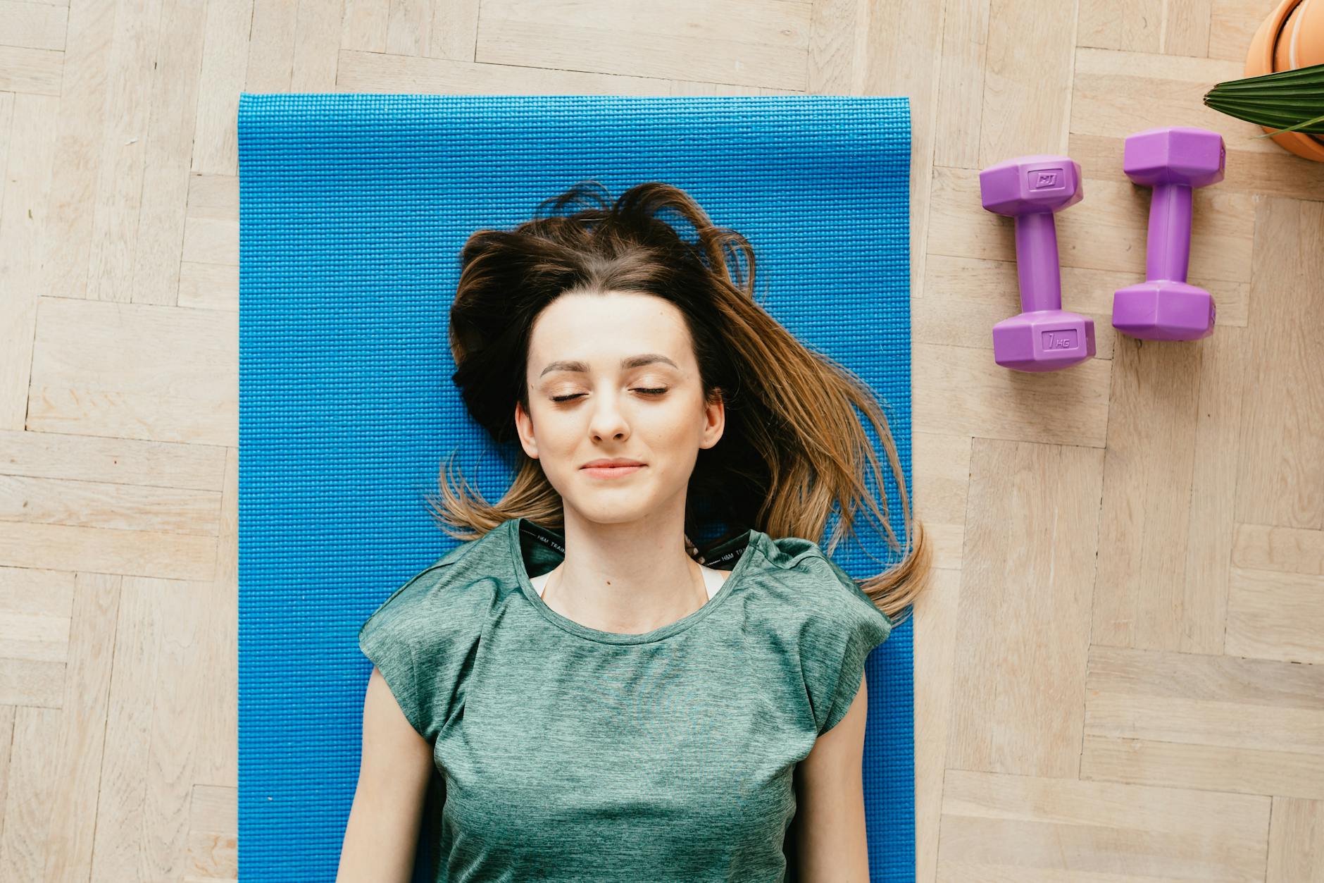 A young woman peacefully resting on a yoga mat with dumbbells beside her indoors.