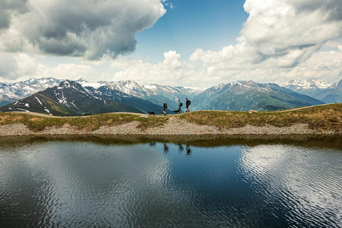 Hikers exploring the picturesque trails of the Austrian Alps with mountain views and reflection in the water.