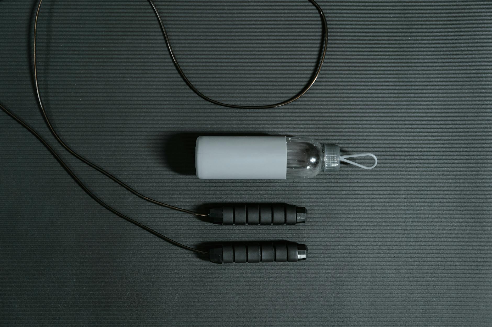Flat lay of jump rope and water bottle on a yoga mat for fitness and hydration.
