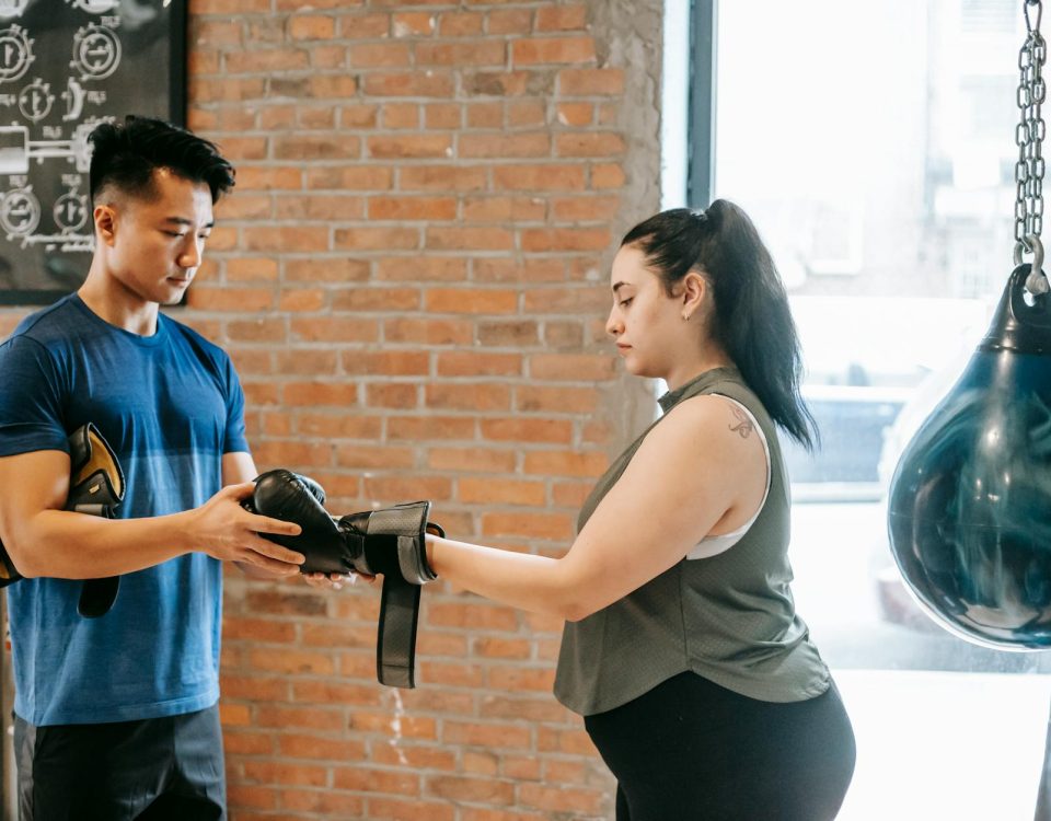 Fitness trainer helping a woman with boxing gloves in an urban gym.