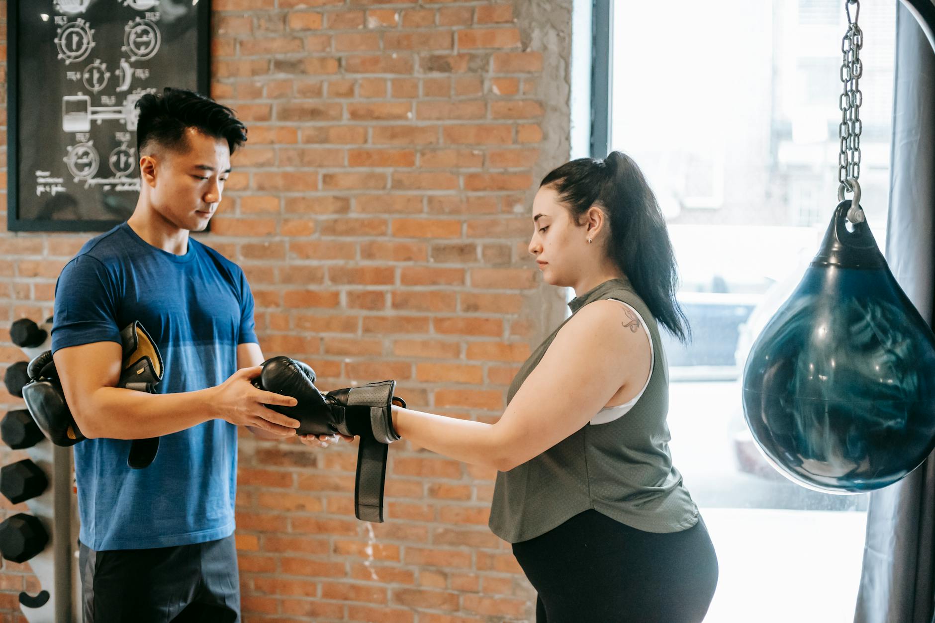 Fitness trainer helping a woman with boxing gloves in an urban gym.